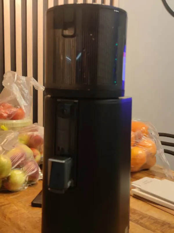 Czarna wyciskarka Hurom H400, obok jabłka i pomarańcze