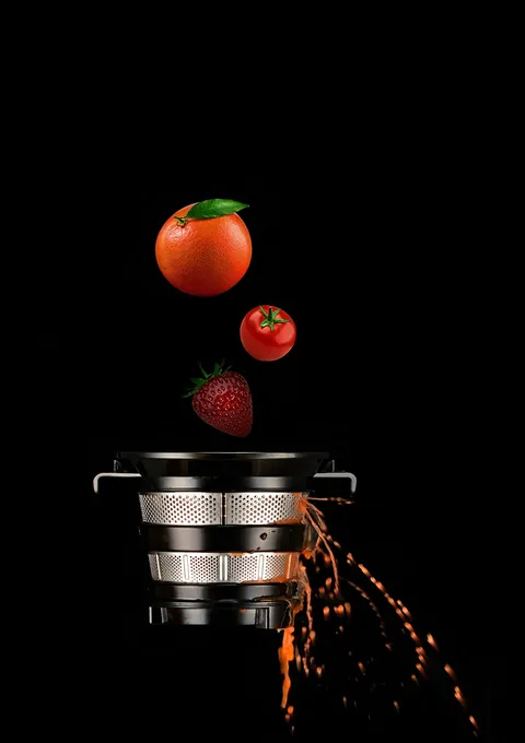 Pomarańcza, pomidor i truskawka wpadają do sitka wyciskarki Hurom E50 ST na czarnym tle