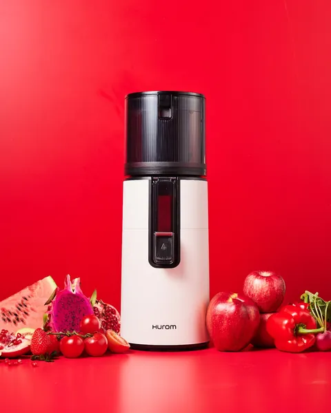 Wyciskarka Hurom H400 w kolorze białym na czerwonym tle wśród czerwonych owoców i warzyw