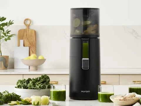 Wyciskarka Hurom H400 w kolorze czarnym na blacie jasnej kuchni z zielonymi sokami i warzywami