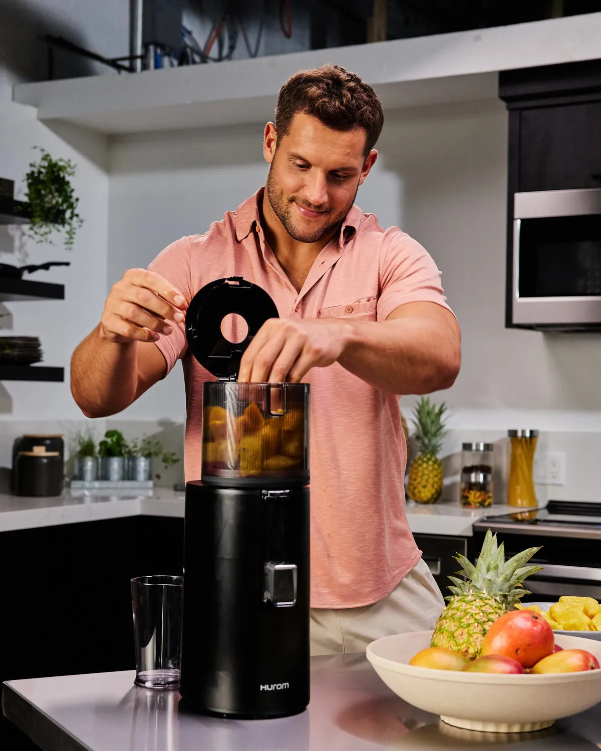 Nick Bosa zakłada pokrywę czarnej wyciskarki Hurom, obok misa z ananasem i owocami