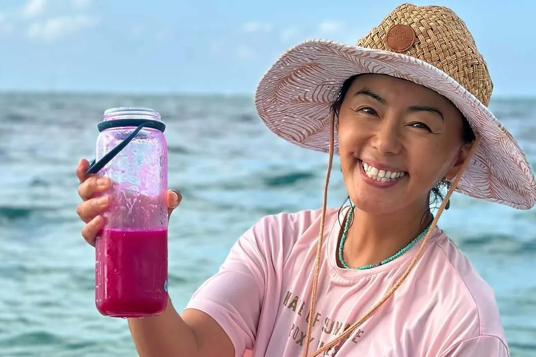 Ritsuko Tanaka w kapeluszu z różowym sokiem w butelce na desce SUP na morzu