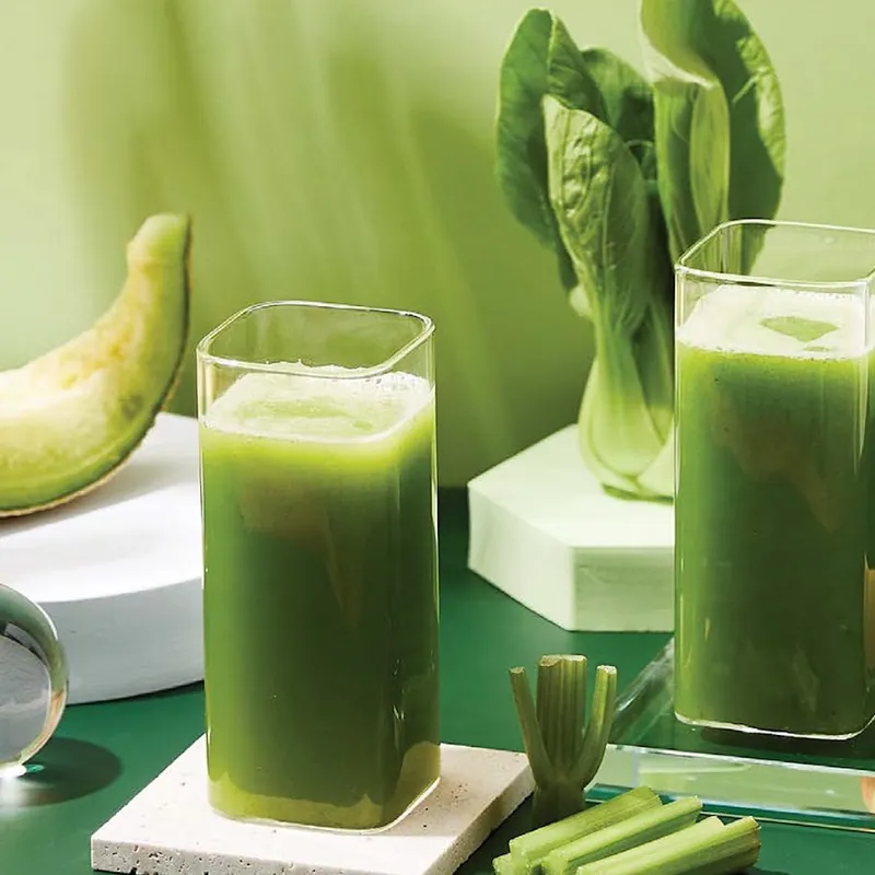 Dwie szklanki zielonego soku z melona i kapusty pak choi na zielonym tle z kawałkami melona